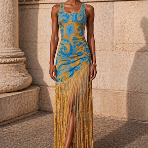 May include: A sleeveless, floor-length dress with a blue and gold floral pattern. The dress features a side slit and a fringe detail at the hem. The model is wearing gold sandals and jewelry.