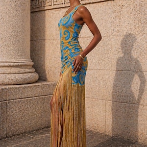 May include: A sleeveless, form-fitting dress with a blue and gold paisley pattern. The dress features a long fringe detail in gold, and is paired with gold high-heeled sandals. The model is wearing gold jewelry.
