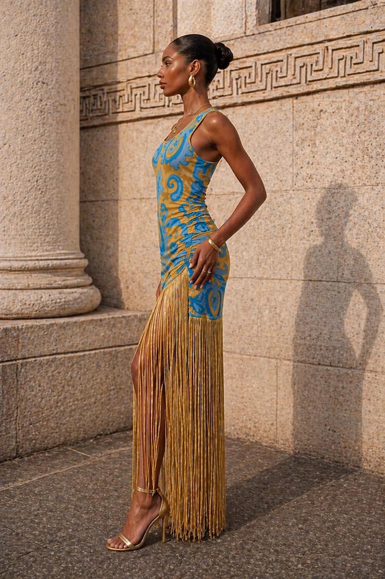 May include: A sleeveless, form-fitting dress with a blue and gold paisley pattern. The dress features a long fringe detail in gold, and is paired with gold high-heeled sandals. The model is wearing gold jewelry.
