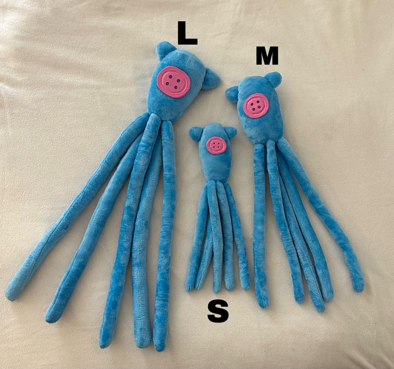 Puede incluir: Tres peluches azules de diferentes tama&ntilde;os, etiquetados L, M y S. Cada juguete tiene un bot&oacute;n rosa en la cara y m&uacute;ltiples ap&eacute;ndices largos y delgados. Los juguetes est&aacute;n colocados sobre una superficie clara.