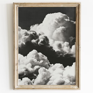 May include: A framed black and white print featuring a dramatic cloudscape. The image showcases large, fluffy clouds against a dark background, creating a striking contrast. The frame is a light gold color, adding a touch of elegance to the artwork.