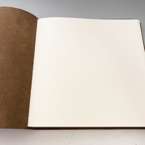 Puede incluir: Un diario encuadernado en cuero marr&oacute;n con p&aacute;ginas blancas en blanco. El diario est&aacute; abierto para revelar las p&aacute;ginas en blanco.