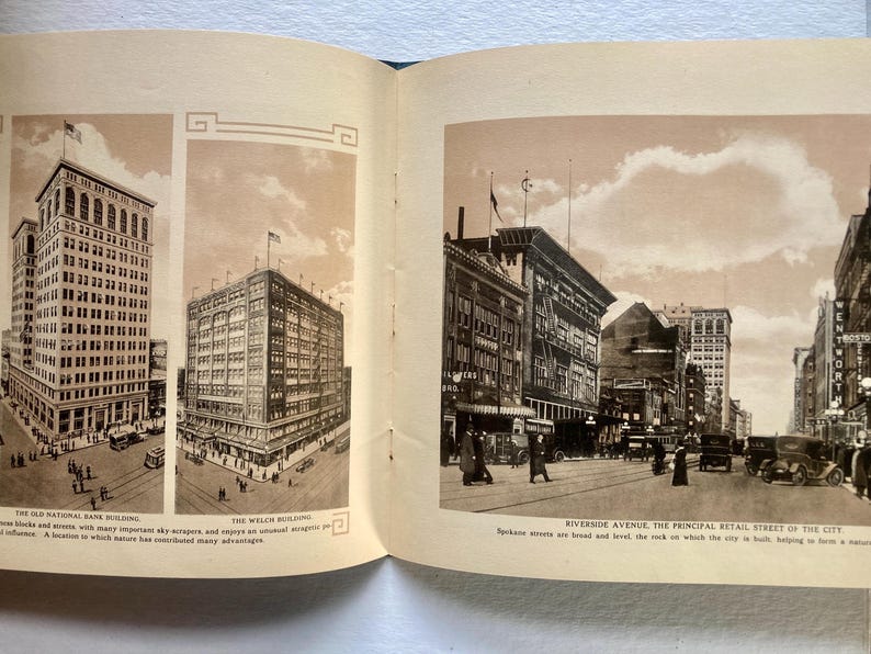 Op de afbeelding: Een vintage zwart-witfoto van een straat in de stad met gebouwen en auto's. De bijschrift luidt "Riverside Avenue, de belangrijkste winkelstraat van de stad. De straten van Spokane zijn breed en vlak, de rots waarop de stad is gebouwd, helpt om haar natuurlijke voordelen te vormen."