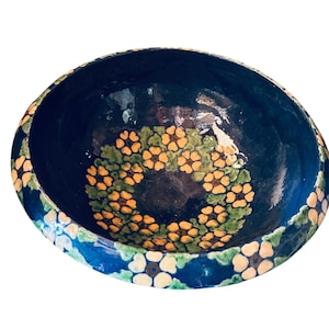 Puede incluir: Un cuenco de cerámica hecho a mano con un interior azul oscuro y un diseño floral. El borde presenta un patrón repetitivo de flores amarillas y blancas sobre un fondo azul. El interior tiene un anillo de flores amarillas.