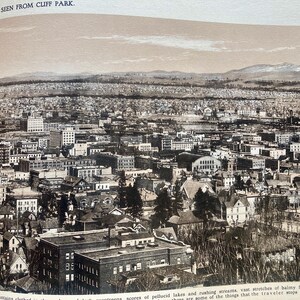 Op de afbeelding: Een zwart-wit luchtfoto van een stad. De stad is dichtbevolkt met gebouwen en bomen. De foto is genomen vanuit een hoog standpunt, waardoor een panoramisch uitzicht op de stad wordt geboden.