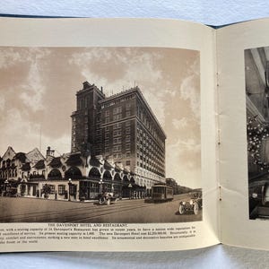 Op de afbeelding: Een zwart-witfoto van een groot hotelgebouw met een bord met de tekst "The Davenport Hotel and Restaurant". Het hotel heeft een grote boogvormige ingang en een rij auto's die ervoor geparkeerd staan.