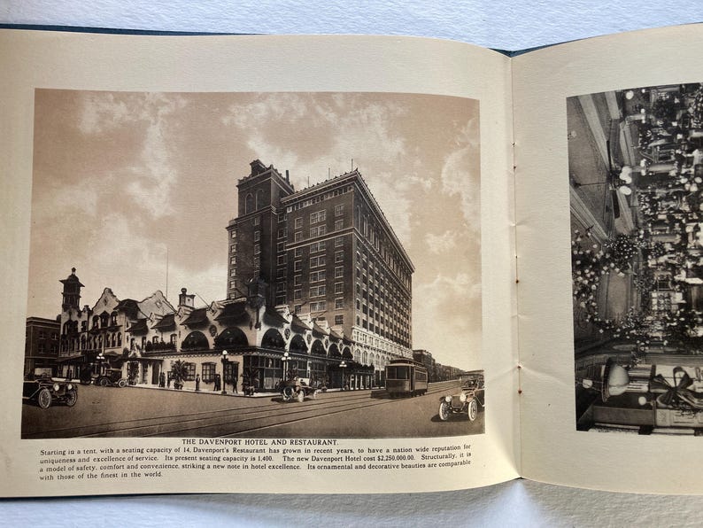 Op de afbeelding: Een zwart-witfoto van een groot hotelgebouw met een bord met de tekst "The Davenport Hotel and Restaurant". Het hotel heeft een grote boogvormige ingang en een rij auto's die ervoor geparkeerd staan.