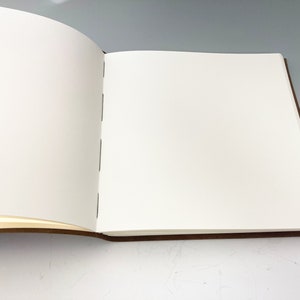 Puede incluir: Un libro blanco abierto, en blanco, con tapas de cuero marr&oacute;n.