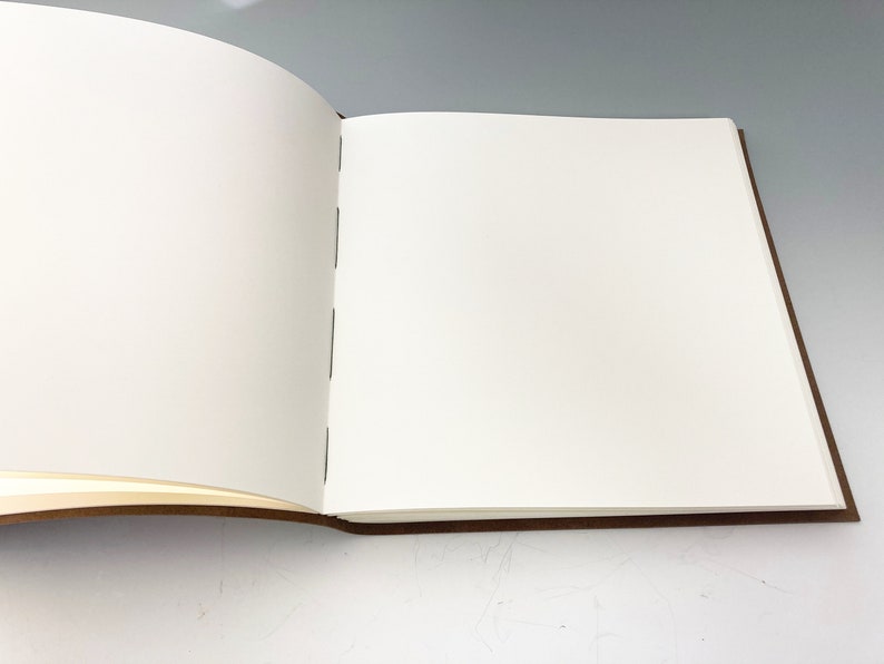 Puede incluir: Un libro blanco abierto, en blanco, con tapas de cuero marr&oacute;n.