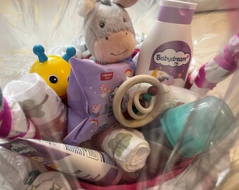 Puede incluir: Una bolsa de plástico transparente llena de artículos para bebés. Incluye un burro de peluche, un juguete amarillo, pañales, loción para bebés, un mordedor de madera y un biberón. La botella de loción tiene el texto "Babydream".