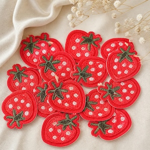 May include: A collection of small, red strawberry-shaped embroidered patches. Each patch features a bright red base with white stitched dots representing seeds and a dark green embroidered stem at the top of the fruit shape.