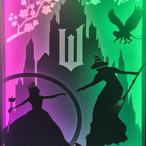 May include: A layered paper art piece with a fantasy theme. Silhouettes of a princess, a witch, and flying monkeys are set against a castle backdrop. The background gradients from pink to green. The princess holds a wand.