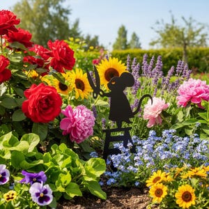 May include: A black metal garden ornament depicting a mouse with scissors, set in a colourful flower bed. The garden features red roses, sunflowers, pink peonies, and blue forget-me-nots, creating a vibrant display.