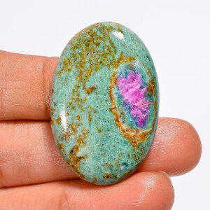 May include: An oval gemstone featuring a teal base with a central splash of pink and blue. The stone has a speckled texture with brown and gold accents. This gemstone is suitable for jewelry making. The stone's dimensions are approximately 3 cm in length.