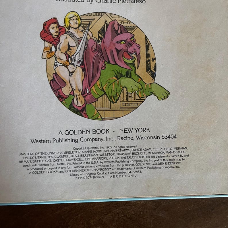 K&ouml;nnte beinhalten: Ein Vintage-Golden-Book-Cover mit Illustrationen von He-Man und anderen Masters-of-the-Universe-Charakteren. Das Kunstwerk zeigt einen muskul&ouml;sen Helden mit einem Schwert, eine Frau mit roter Kapuze und ein gr&uuml;nes Monster.