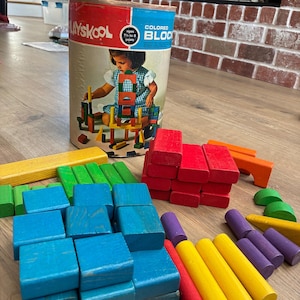 May include: A vintage Playskool colored block set featuring a cylindrical cardboard container with a child illustration and text. The set includes various wooden building blocks in red, blue, green, yellow, orange, and purple, with shapes including cubes, rectangular prisms, cylinders, and semi-circles.