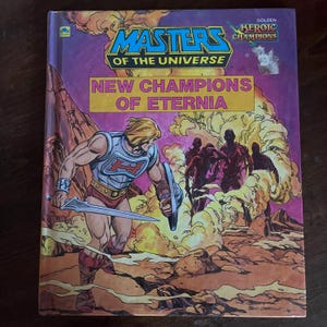 K&ouml;nnte beinhalten: Ein Vintage-Comicbuch "Masters of the Universe". Das Cover zeigt eine muskul&ouml;se Figur mit Schwert und Schild vor einer felsigen Landschaft und einer Gruppe von Silhouetten. Der Titel "New Champions of Eternia" ist deutlich sichtbar.