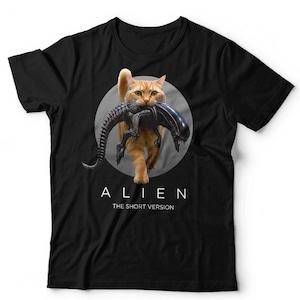 May include: Black t-shirt featuring a ginger cat carrying an Alien creature graphic. The cat is centered on a gray circle. The word "ALIEN" is printed above "THE SHORT VERSION" in white.