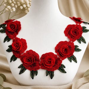 Peut inclure: Une application en dentelle décorative composée d'une série de roses brodées rouge vif avec des feuilles vert foncé détaillées. L'arrangement floral est conçu pour suivre la forme d'une encolure, avec des coutures et des pétales superposés.