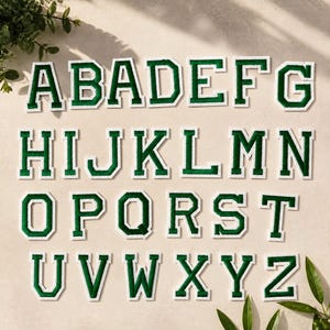 Könnte beinhalten: Ein vollständiger Satz von sechsundzwanzig Buchstaben des Alphabets von A bis Z in einer Schriftart im College-Stil. Jeder Buchstabe besteht aus einem dunkelgrünen Filzkern mit einem dicken weißen Rand und ist als Aufbügler für Textilien gedacht.
