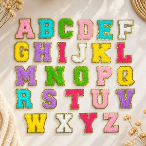 Peut inclure: Un ensemble complet de vingt-six écussons en forme de lettres de l'alphabet avec une surface texturée en chenille duveteuse dans des couleurs vives comme le rose, le bleu, le vert, le jaune, le violet et le blanc, bordés de paillettes dorées.