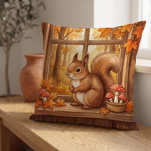 May include: A square throw pillow featuring a printed illustration of a brown squirrel sitting on a wooden windowsill. The scene includes orange autumn leaves, a small woven basket filled with red and white spotted mushrooms, and a window view.