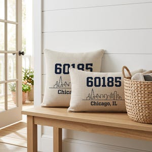 Peut inclure: Deux coussins décoratifs beiges avec une finition en tissu texturé. Chaque coussin présente le texte bleu foncé 60185, une illustration en ligne noire de la ligne d'horizon et le texte Chicago, IL imprimés sur la face avant des coussins.