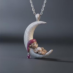 Könnte beinhalten: Ein Anhänger in Form einer Mondsichel, besetzt mit weißen Steinen. Eine kleine Bärenfigur aus braunen Steinen sitzt auf dem Mond und trägt eine mit roten Steinen besetzte Schlafmütze. Ein einzelner tropfenförmiger roter Stein hängt am Mond.