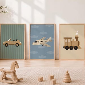 Op de afbeelding: Een set van drie ingelijste wandposters met transportthema's. De eerste poster toont een beige cabriolet op een groen gestreepte achtergrond. De tweede toont een beige vliegtuig in een blauwe lucht met wolken. De derde toont een beige stoomtrein.