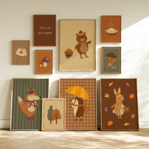 Peut inclure: Un ensemble de dix affiches encadrées sur le thème de l'automne, illustrant un ours avec une citrouille, un hérisson avec un parapluie, un renard, un lapin, des champignons, une tarte, des arbres et un pull, avec le texte HELLO AUTUMN.