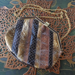 May include: Vintage snakeskin clutch with a gold chain strap. The purse features vertical panels of brown, tan, and black snakeskin. The frame is a dark brown with a gold clasp. A stylish accessory for any occasion.