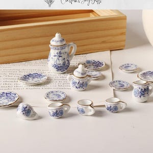 May include: A miniature porcelain tea set featuring blue floral patterns. The set includes a teapot, cups, saucers, and a creamer. The pieces are white with blue floral designs and gold trim. The set is displayed on a light-colored surface.