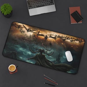 Puede incluir: Alfombrilla de escritorio negra con diseño de arte fantástico. La imagen muestra una figura con capa oscura y tocado con cuernos, con criaturas voladoras contra un cielo tormentoso. También se ve un ratón blanco y un portátil.