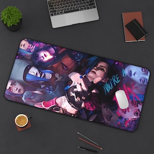 Puede incluir: Alfombrilla de ratón rectangular con una ilustración vibrante de un personaje con cabello azul y el texto "YOU'RE A". El diseño incluye múltiples rostros en tonos morados, rosas y azules. Un ratón blanco descansa sobre la alfombrilla.