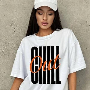 Puede incluir: Camiseta blanca con la palabra "CHILL Out" en letras negras y naranjas. La modelo lleva una gorra de béisbol blanca con texto. La camiseta se combina con pantalones cortos vaqueros. El fondo es una pared gris.