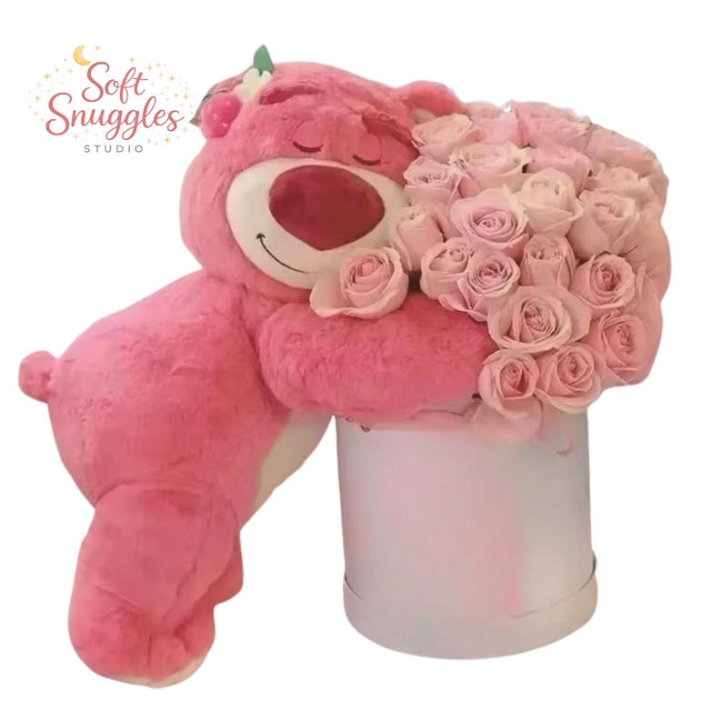 May include: A large pink plush bear embraces a bouquet of light pink roses in a white round box. The bear has a smiling face and is holding the flowers. The image includes the text "Soft Snuggles STUDIO".