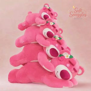 May include: A stack of pink plush bear toys with white and dark pink accents. Each bear has a flower crown and closed eyes. The image includes the text "Soft Snuggles Studio" in a cursive font.