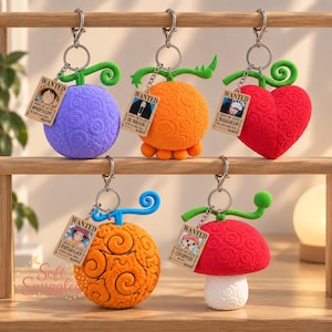 May include: Five plush keychains shaped like fantasy fruits with swirling patterns, each featuring a metal lobster clasp and a small rectangular tag labelled WANTED with a character portrait and bounty text, including purple, orange, red, and white colours.