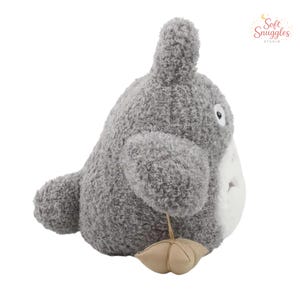 May include: A plush gray character with a white belly, large ears, and a small tan accessory. The stuffed animal has a soft, textured appearance and a friendly expression. The product is from Soft Snuggles Studio.
