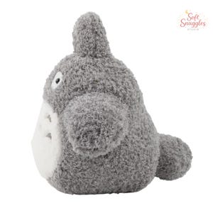 May include: A gray plush toy resembling a character from an animated film. The stuffed animal has a rounded body, small ears, and a white belly. The toy is made of soft, fuzzy material and has a friendly expression.