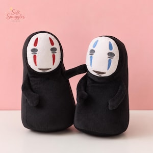May include: Two plush toys resembling the character No-Face from the animated film Spirited Away. The black figures have white faces with red and blue markings. The Soft Snuggles Studio logo is in the upper left corner.