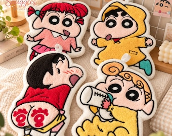 Może przedstawiać: Cztery tuftowane podkładki tekstylne z postaciami z Crayon Shin-chan. Jedna przedstawia dziewczynkę w różu, druga chłopca w żółtym płaszczu przeciwdeszczowym, trzecia schylonego chłopca, a czwarta niemowlę z butelką. Każda ma białą pętelkę.