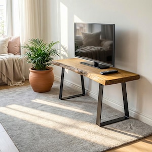 Könnte beinhalten: Ein TV-Ständer aus Holz mit einem Design mit lebendiger Kante und schwarzen Metallbeinen. Ein Flachbildfernseher steht auf dem Ständer, mit einer Fernbedienung davor. Eine Topfpflanze und ein Teppich befinden sich im Vordergrund und schaffen eine gemütliche Wohnzimmeratmosphäre.