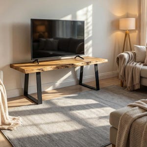 Può includere: Un mobile TV in legno con piano a bordo vivo e gambe in metallo nero. La venatura naturale del legno è visibile sul piano. Un grande televisore a schermo piatto è posto sopra il supporto. Il supporto si trova in un soggiorno.