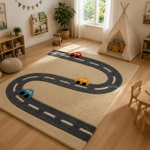 May include: A rectangular area rug featuring a beige background with a dark gray winding road pattern. The road includes white dashed lane markings and three small toy cars in red, yellow, and blue colors positioned along the path.