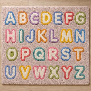 May include: A rectangular area rug with a light pink textured surface featuring the English alphabet in capital letters. Each letter is rendered in a puffy, tufted style with a white center and a colorful border in shades of blue, orange, purple, yellow, red, green, and pink.