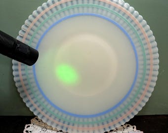 May include: A white milk glass plate with a scalloped edge and three bands of blue, green, and pink around the rim.