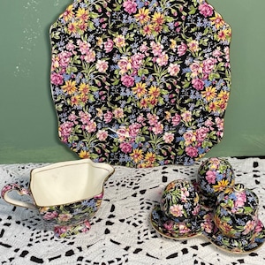 Può includere: Un set da tè floreale bianco e nero con un piatto da portata quadrato, una brocca per la panna e un set di saliera e pepe. Il set presenta un motivo floreale con fiori rosa, gialli e blu.