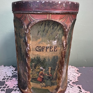 以下が含まれることがあります： 蓋と装飾的なハンドルが付いた、ヴィンテージの金属製コーヒー缶。缶には人物と「COFFEE」の文字が描かれた風景画が描かれています。カラーパレットには、赤、緑、茶色の色合いが含まれています。