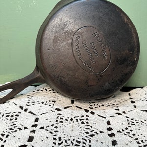 May include: A vintage cast iron skillet with a black handle. The skillet has a round, embossed logo that reads "Keystone Food Chopper Boyertown, PA".